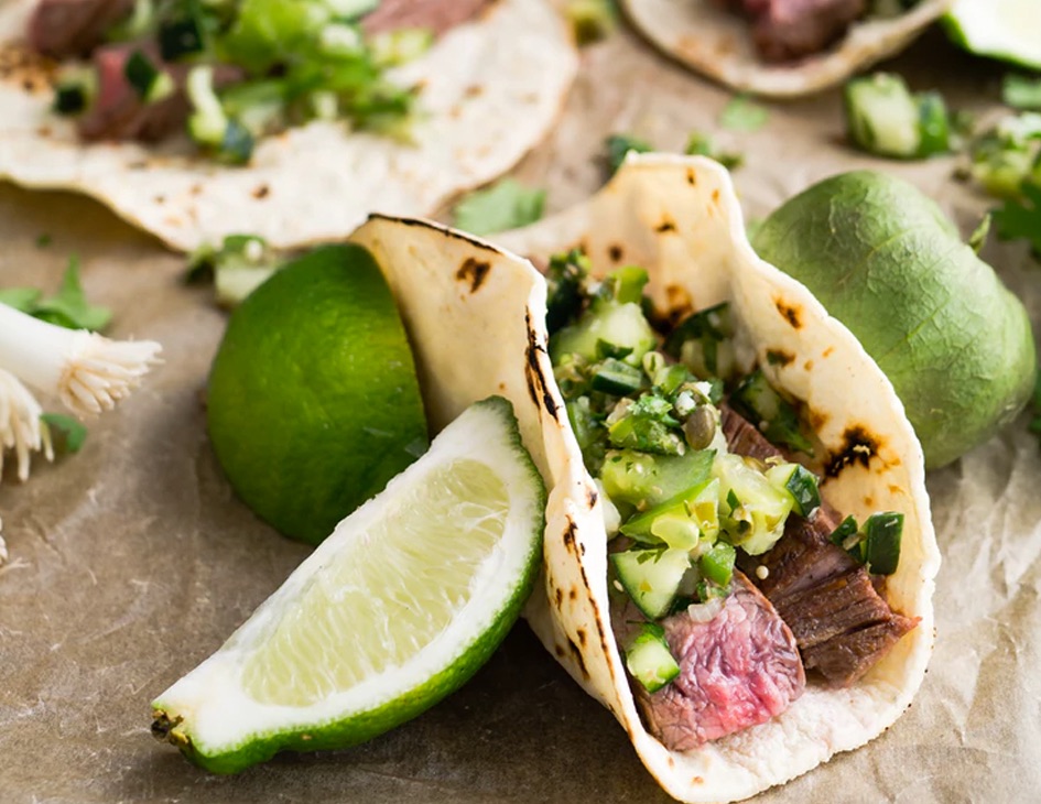 A steak taco next to some lime wedges.